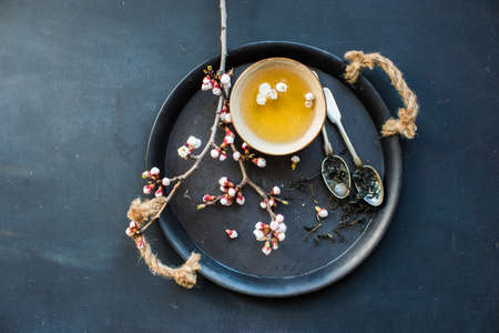 Cup of green tea and peach blossom on dark rustic table as a spring time conceptの写真素材