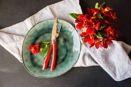 Summer table setting with red lily flowers on bright colored plates on dark rustic wooden table