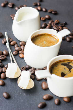 Mug with black coffee, coffee beans, milk and sugar on dark wooden tableの写真素材