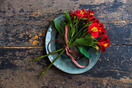 Summer table setting with red lily flowers on bright colored plates on dark rustic wooden tableの写真素材