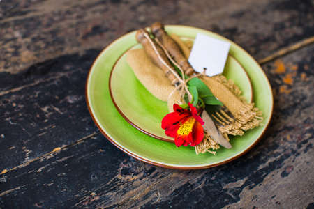 Summer table setting with red lily flowers on bright colored plates on dark rustic wooden table