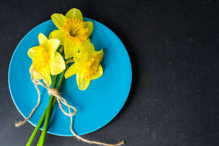 Spring table setting for Easter dinner with bright plates and bright yellow daffodils on a wooden...