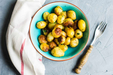 Roast potatoes seasoned with salt, garlic and provance herbs in rustic ceramic bowl on grey concrete backgroundの写真素材