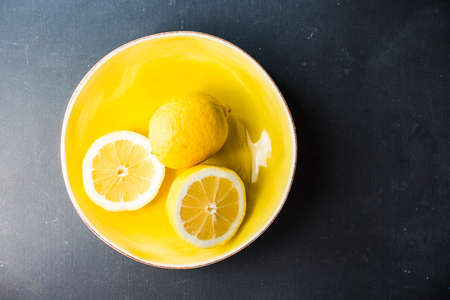 Fresh organic lemons in a bright yellow ceramic bowl on dark backgroundの写真素材