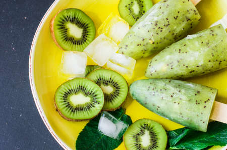 Summer fruit dessert - kiwi lollipops with mint and ice on rustic plate on concrete backgroundの写真素材