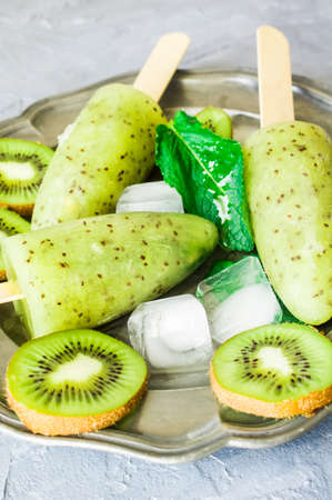 Summer fruit dessert - kiwi lollipops with mint and ice on rustic plate on concrete backgroundの写真素材