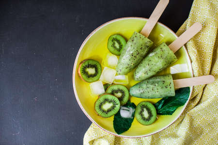 Summer fruit dessert - kiwi lollipops with mint and ice on rustic plate on concrete backgroundの写真素材