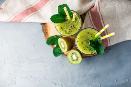 Organic food concept of fresh kiwi smoothie on grey concrete background with fruits and mintの写真素材