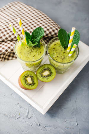 Organic food concept of fresh kiwi smoothie on grey concrete background with fruits and mintの写真素材