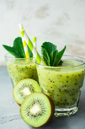 Organic food concept of fresh kiwi smoothie on grey concrete background with fruits and mintの写真素材