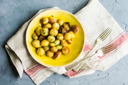 Roast potatoes seasoned with salt, garlic and provance herbs in rustic ceramic bowl on grey concrete backgroundの写真素材