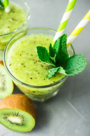 Organic food concept of fresh kiwi smoothie on grey concrete background with fruits and mintの写真素材