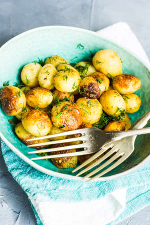 Roast potatoes seasoned with salt, garlic and provance herbs in rustic ceramic bowl on grey concrete backgroundの写真素材
