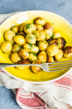 Roast potatoes seasoned with salt, garlic and provance herbs in rustic ceramic bowl on grey concrete backgroundの写真素材