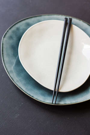 Ceramic plate and black wooden chopsticks for dinner in asian restaurant