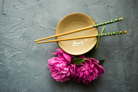 Summer table setting for dinner with asian dishes with bright peonies on dark rustic table with copyspaceの写真素材