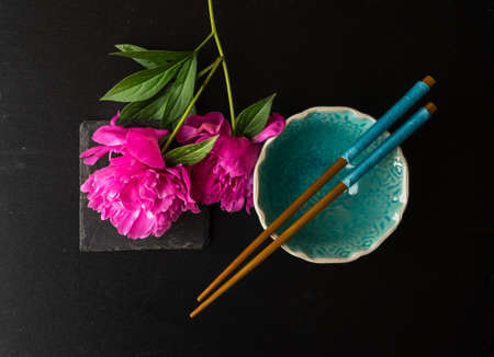 Summer table setting for dinner with asian dishes with bright peonies on dark rustic table with copyspaceの写真素材
