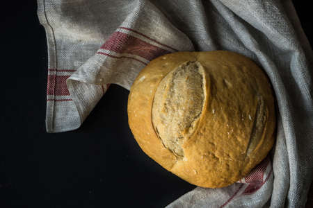 Freshbaked homemade bread on a towel on dark wooden tableの写真素材