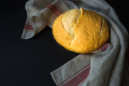 Freshbaked homemade bread on a towel on dark wooden table