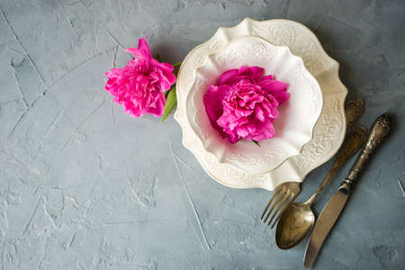 Summer table setting with bright peonies on dark rustic table with copyspace