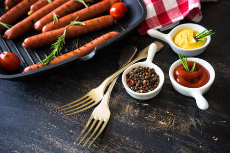 Unhealthy food - grilled sausages with rosemary and tomatoes on dark wooden tableの写真素材