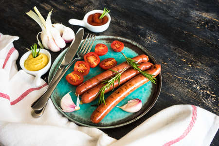 Unhealthy food - grilled sausages with rosemary and tomatoes on dark wooden tableの写真素材