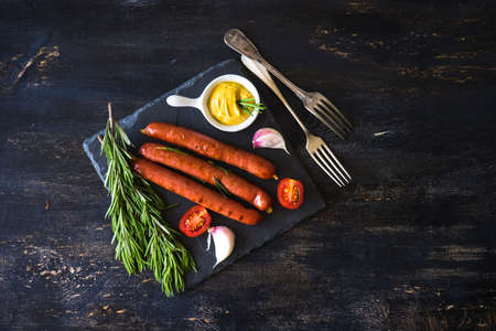 Unhealthy food - grilled sausages with rosemary and tomatoes on dark wooden tableの写真素材