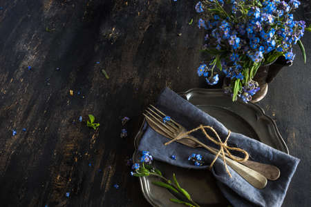 Summer floral table setting with bright blue forget-me-not flowers on wooden tableの写真素材