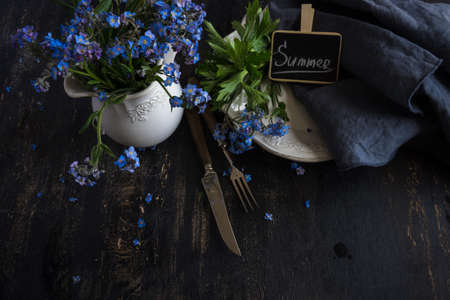 Summer floral table setting with bright blue forget-me-not flowers on wooden tableの写真素材