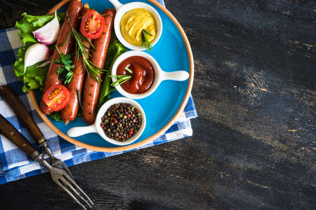 Unhealthy food - grilled sausages with rosemary and tomatoes on dark wooden tableの写真素材
