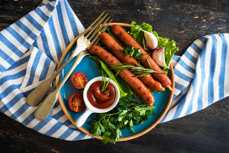 Unhealthy food - grilled sausages with rosemary and tomatoes on dark wooden tableの写真素材