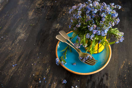 Summer floral table setting with bright blue forget-me-not flowers on wooden tableの写真素材