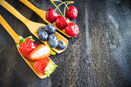 Summer fruits on spoons on wooden background with copyspaceの写真素材