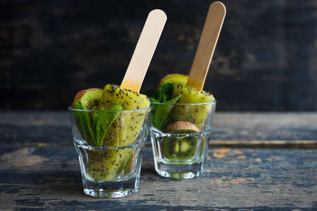 Summer fruit dessert - kiwi lollipops with mint and ice on rustic plate on concrete background