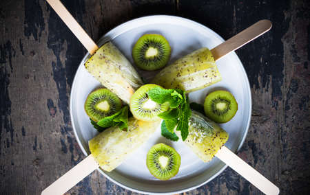Summer fruit dessert - kiwi lollipops with mint and ice on rustic plate on concrete backgroundの写真素材