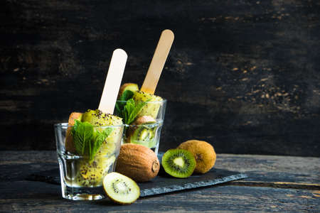 Summer fruit dessert - kiwi lollipops with mint and ice on rustic plate on concrete backgroundの写真素材