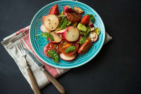 Spring healthy salald with fresh organic tomatoes, radish and rukkola herb on rustic plate with napkin and silverwareの写真素材