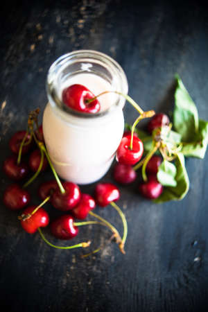 Bottle with yogurt and cherries on dark wooden table with copyspaceの写真素材