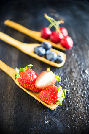 Summer fruits on spoons on wooden background with copyspaceの写真素材