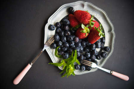 Plate with fresh organic strawberries and blueberries on dark wooden table with copyspace
