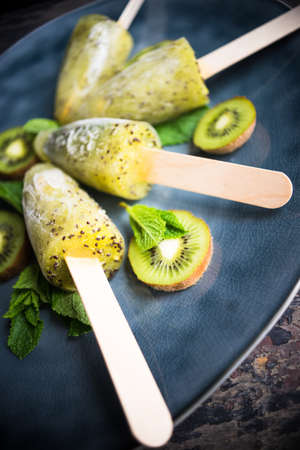 Summer fruit dessert - kiwi lollipops with mint and ice on rustic plate on concrete backgroundの写真素材