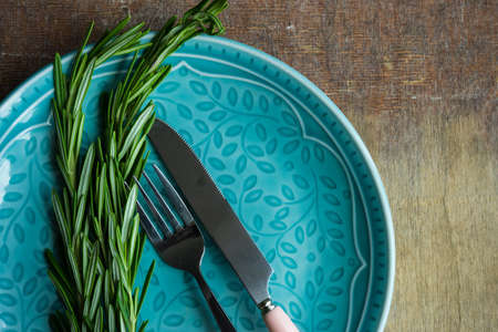Summer table setting with bright blue plate and fresh rosemary on vintage wooden tableの写真素材