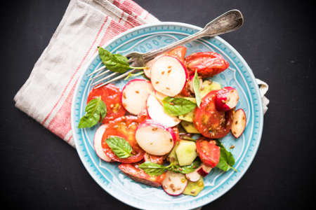 Spring healthy salald with fresh organic tomatoes, radish and rukkola herb on rustic plate with napkin and silverwareの写真素材
