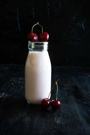 Bottle with yogurt and cherries on dark wooden table with copyspaceの写真素材
