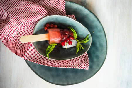 Summer fruit dessert - strawberry lollipops with mint and ice on rustic plate on concrete backgroundの写真素材