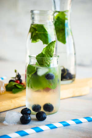 Detox summer drinks with fresh mint leaves and berries on white rustic wooden tableの写真素材