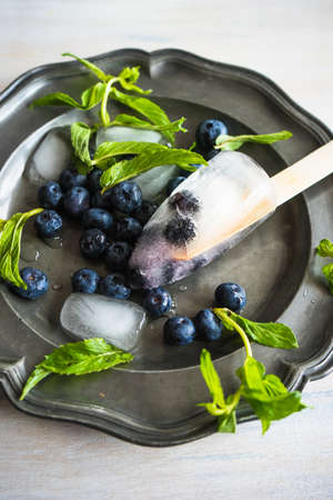 Summer fruit dessert - bilberry lollipops with mint and ice on rustic plate on concrete background
