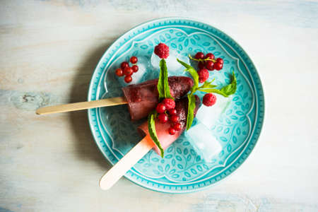 Summer fruit dessert - strawberry lollipops with mint and ice on rustic plate on concrete backgroundの写真素材