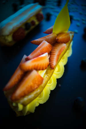 Different eclair dessert on dark wooden table decorated with strawberries and flowers