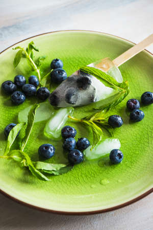 Summer fruit dessert - bilberry lollipops with mint and ice on rustic plate on concrete backgroundの写真素材